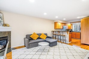 A modern living room with a grey sectional sofa, two yellow cushions, a white coffee table, and a patterned rug. - Corner 3BR - Fireplace - Balcony - Washer Dryer (Seattle)