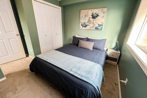 A bedroom with a bed, a nightstand, a wall-mounted painting, and a door. - Corner 3BR - Fireplace - Balcony - Washer Dryer (Seattle)