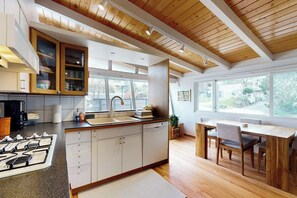 A modern kitchen with a central island, wooden ceiling beams, and large windows providing natural light. - 1BR Home- Tranquil Mid-Century retreat (Seattle)