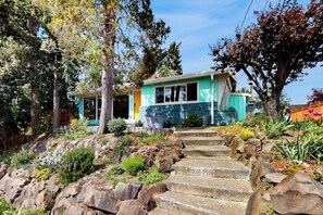 A two-story house with a stone staircase leading to the front door, surrounded by a garden with various plants and trees. - 1BR Home- Tranquil Mid-Century retreat (Seattle)