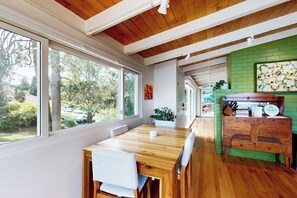 A dining area with a wooden table and chairs, a green brick wall, and a view of the outdoors. - 1BR Home- Tranquil Mid-Century retreat (Seattle)