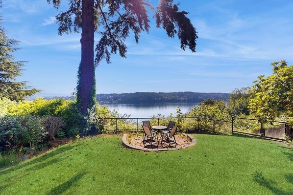 A backyard with a lawn, a table with chairs, and a view of a lake. - 2BR Lakefront home with deck & garage parking (Lake Forest Park)