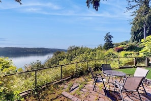 Eine Terrasse mit Sitzgelegenheiten im Freien mit Blick auf einen See, umgeben von üppiger Vegetation und blauem Himmel.