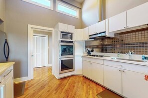 Une cuisine moderne avec des meubles blancs, un four double, un four à micro-ondes et un dosseret carrelé.