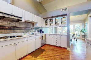 A modern kitchen with white cabinetry, a stainless steel range hood, and a wooden floor. - 2BR Lakefront home with deck & garage parking (Lake Forest Park)