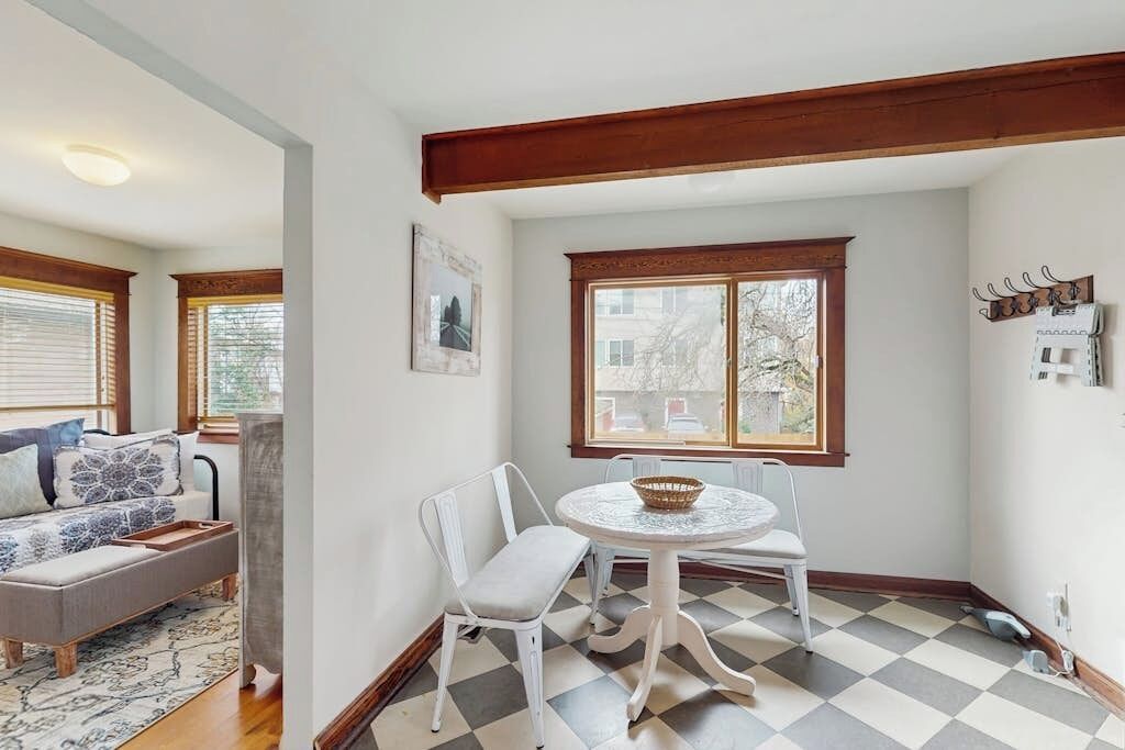 A dining area with a round table and chairs, a window with a view, and a checkered floor.