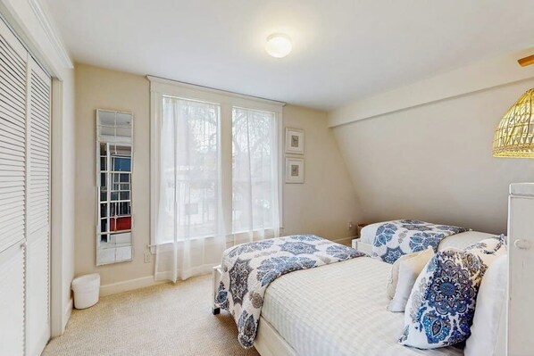 Een slaapkamer met twee bedden, een raam met dunne gordijnen, een plafondlamp en een wandlamp.