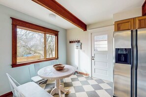 Uma cozinha com piso xadrez, geladeira, janela com vista e mesa com cadeiras.
