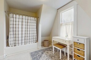 Ein Badezimmer mit Duschvorhang, einem kleinen Schreibtisch mit Schubladen, einem Stuhl und einem Fenster.