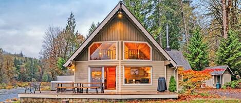 A cabin with a large deck, a fireplace, and a view of the forest.