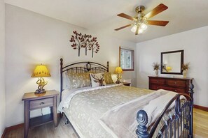 Ein Schlafzimmer mit Bett, Nachttischen, Deckenventilator, Wandspiegel und dekorativen Wandbildern.