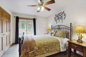 Un dormitorio con cama, mesita de noche, lámpara, ventilador de techo y ventana con cortinas.