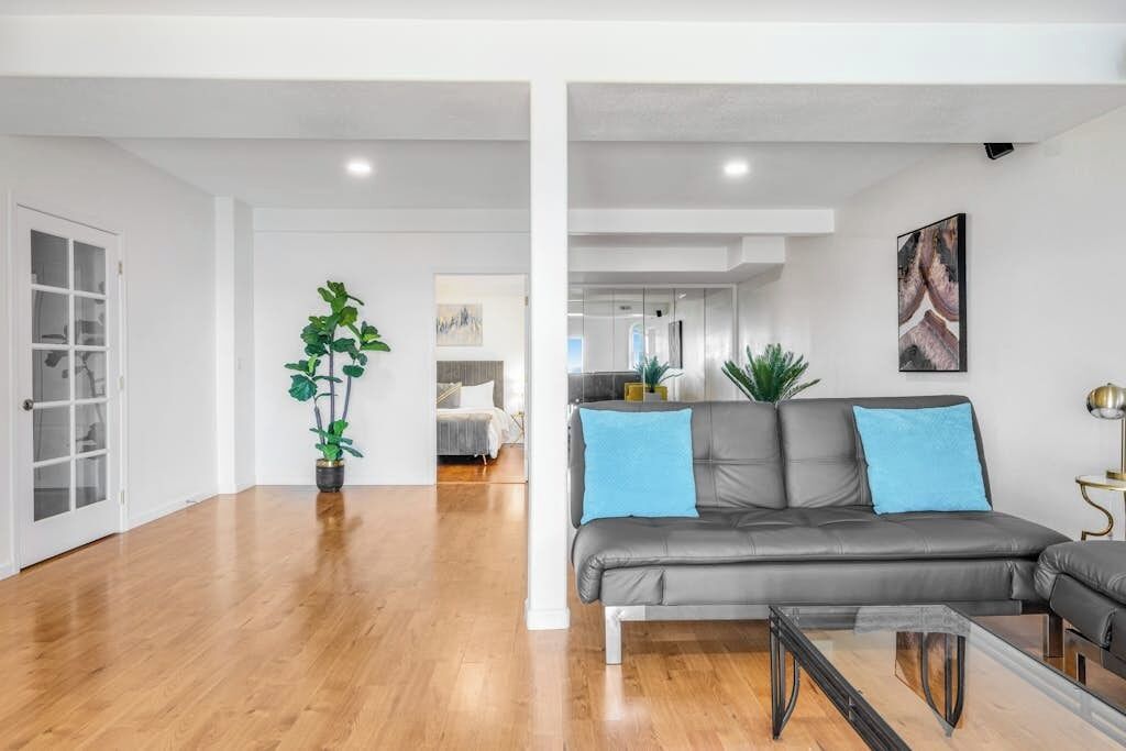 A modern living room with a grey sofa, two blue cushions, a glass coffee table, and a potted plant.