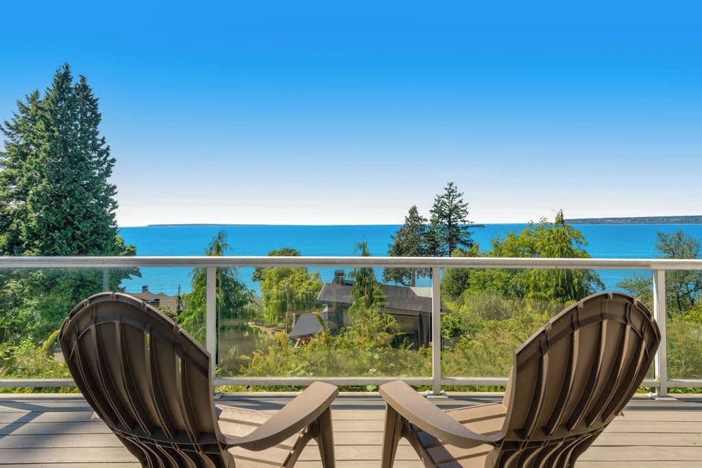A deck with two chairs facing a clear blue sky and a body of water.