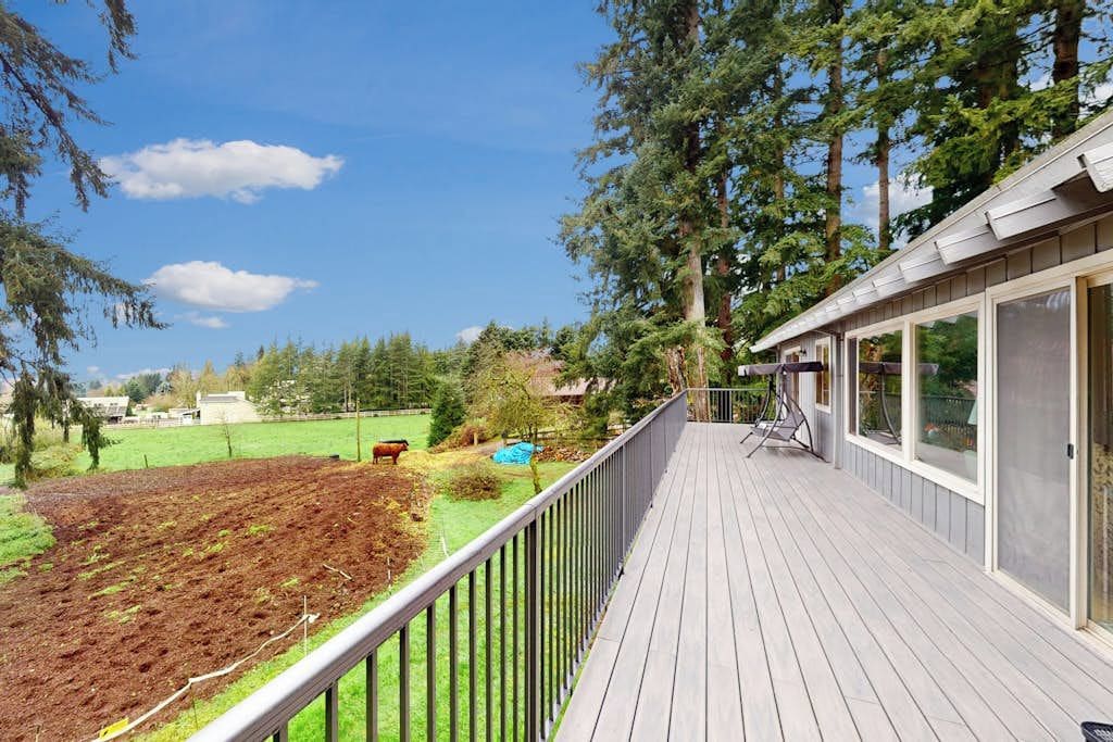 A wooden deck with a metal railing, overlooking a landscaped garden and a clear blue sky.