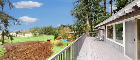 A wooden deck with a metal railing, overlooking a landscaped garden and a clear blue sky.