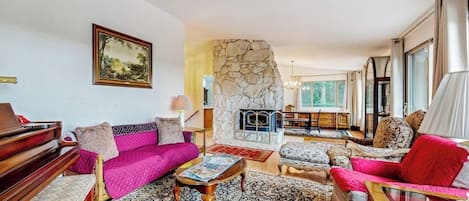 A living room with a stone fireplace, a piano, and a sofa with a red cushion.