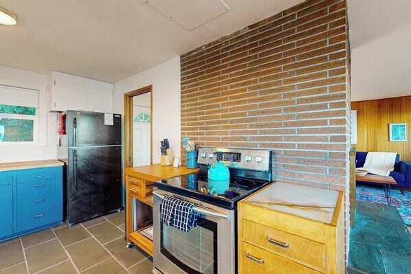 Eine kleine Küche mit Kühlschrank, Backofen und einem blauen Wasserkocher auf dem Herd.
