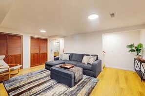 A living room with a sofa, ottoman, and a striped rug. There is a wooden door and a plant on a side table. - 2BR Vashon Island Home with Breathtaking views (Vashon)