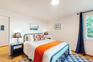 Ein Schlafzimmer mit Bett, Nachttischen, einem Fenster mit Vorhängen und Bildern an den Wänden.