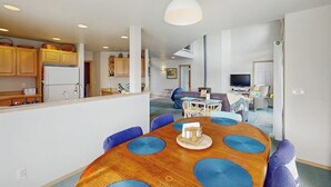 Una cocina moderna con armarios de madera, una isla central y una zona de comedor con una mesa redonda y sillas azules.