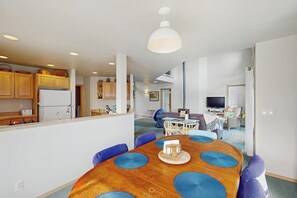 Een moderne keuken met houten kastjes, een centraal eiland en een eetgedeelte met een ronde tafel en blauwe stoelen.