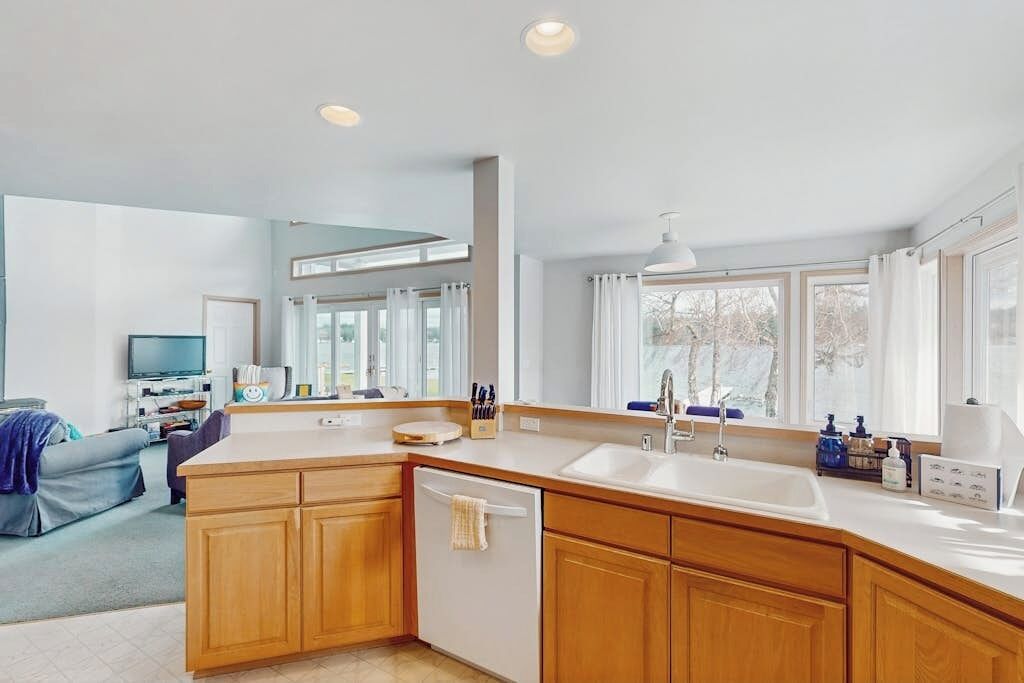 A modern kitchen with wooden cabinets, a built-in dishwasher, and a large window providing natural light.