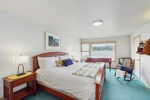 Een slaapkamer met een bed, nachtkastjes, een schommelstoel, een bureau en een raam met uitzicht.