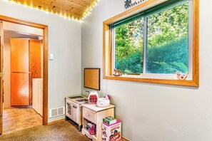 Ein Zimmer mit Fenster, Holztür, einer kleinen Küchenzeile und einem Spielbereich für Kinder.
