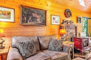 Ein gemütliches Zimmer mit einer Holzwand, einem roten Herd und einer Couch mit gemusterten Kissen.