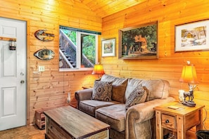 L’intérieur chaleureux d’un chalet, avec un revêtement mural en bois, un canapé, une table basse et une lampe.