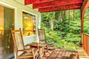 Eine Holzterrasse mit zwei Schaukelstühlen und einem Tisch, mit Blick auf eine bewaldete Gegend.