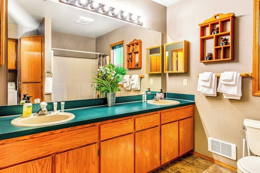 A bathroom with wooden cabinets, a large mirror, a sink, and a toilet.