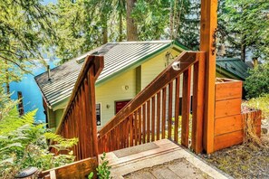 A wooden staircase leading to a cabin with a green roof, surrounded by trees and a body of water. - Stunning 1BR Lakefront Dog Friendly - Hot Tub (Port Angeles)