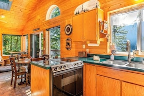 A wooden cabin interior with a kitchen, dining area, and a large window overlooking a forest. - Stunning 1BR Lakefront Dog Friendly - Hot Tub (Port Angeles)