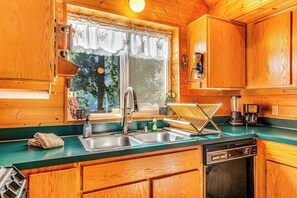 Une cuisine rustique, située dans une cabane en bois, équipée d’un évier, d’une machine à café et d’un lave-vaisselle.