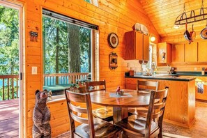 A wooden cabin interior with a dining area, kitchen, and a large window overlooking a forest. - Stunning 1BR Lakefront Dog Friendly - Hot Tub (Port Angeles)
