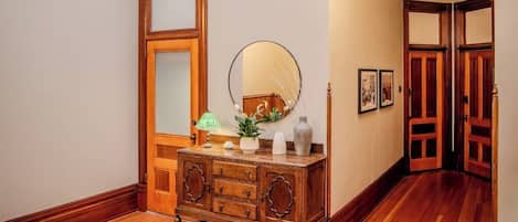 A wooden dresser with a mirror, a lamp, and decorative items. There is a rug on the floor and a hallway leading to a door.