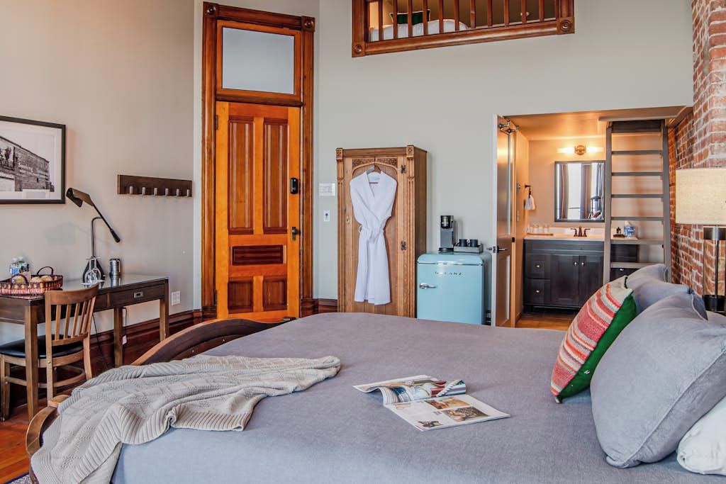 A bedroom with a bed, a desk, a chair, a wardrobe, and a kitchenette.