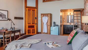 A bedroom with a bed, a desk, a chair, a wardrobe, and a kitchenette.
