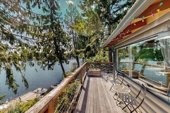 A wooden deck with a glass railing overlooking a lake, surrounded by trees.