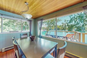 A dining area with a table and chairs, a view of a lake, and a deck with chairs.