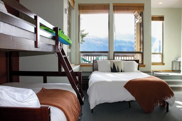 A room with bunk beds, a balcony with a view, and large windows.
