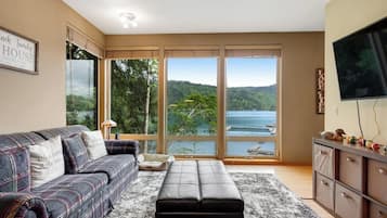 A living room with a sofa, a bench, a TV, and a view of a lake.