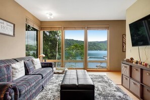 A living room with a sofa, a bench, a TV, and a view of a lake.