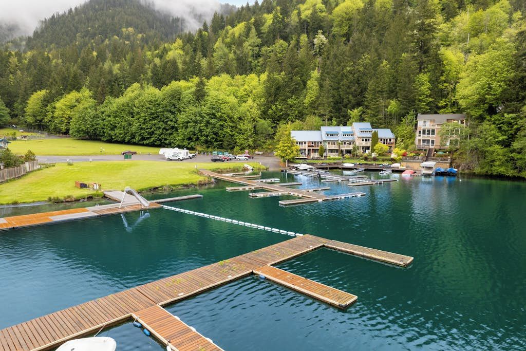 A lakeside hotel with docked boats, a grassy area, and forested hills in the background.