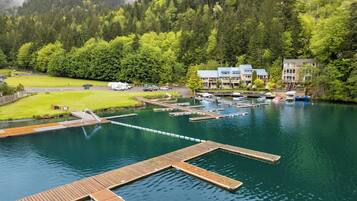 A lakeside hotel with docked boats, a grassy area, and forested hills in the background.