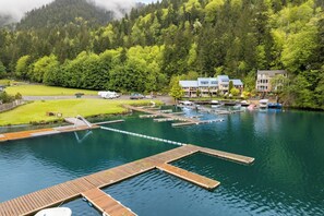 A lakeside hotel with docked boats, a grassy area, and forested hills in the background.