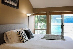 A bedroom with a bed, pillows, a lamp, and a view of the outdoors.