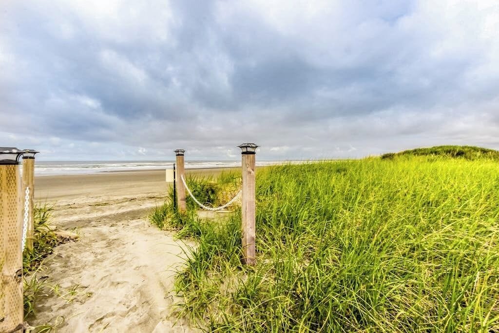 A pathway leading to a beach with a chain-link fence and wooden posts.